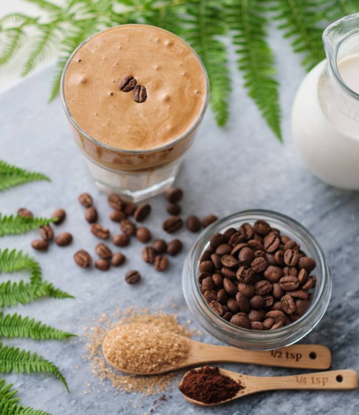 Top view of dalgona coffee with almond milk and brown sugar, co Top view of dalgona coffee with almond milk and brown sugar, coffee beans and green plant on marble board. A glass of trendy fluffy Korean drink with whipped cream.